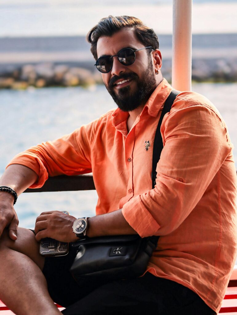 Man wearing sunglasses sitting by the sea, enjoying a sunny seaside vacation.