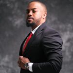 Portrait of a confident man wearing a black suit and red tie, looking assertive.