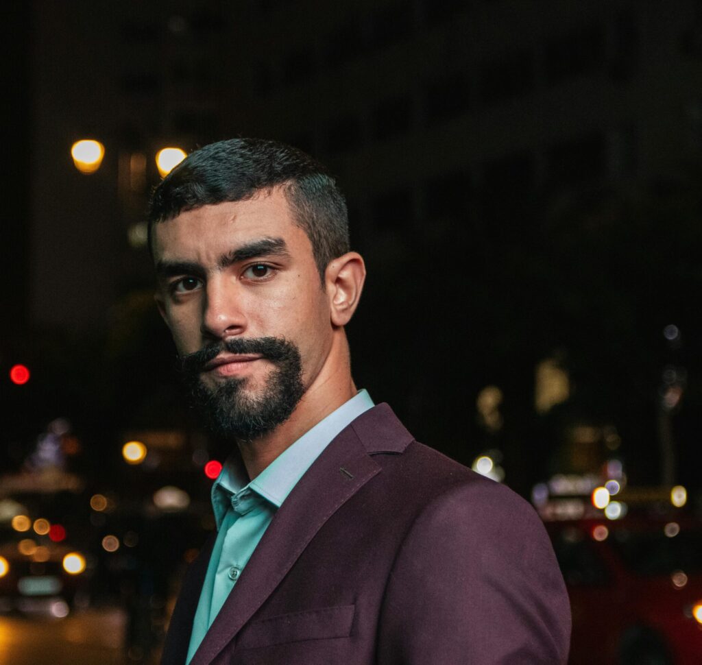 Confident man in a formal suit poses against a vibrant city night backdrop, showcasing urban style.
