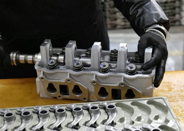 Mechanic assembling an engine cylinder head with precision components on a workbench.