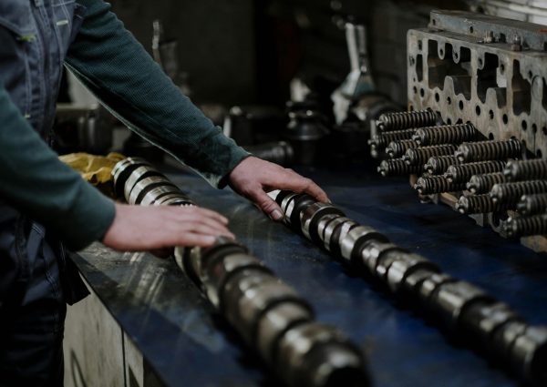 Worker handling camshafts and cylinder head in a mechanic workshop.