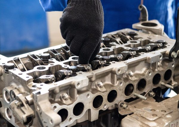 Close-up of a mechanic in gloves working on a car engine cylinder head in a workshop setting.